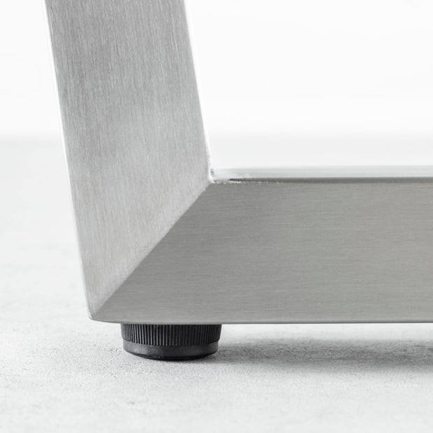 KANADEMONOの配線孔BROCK&TRAY付きのラバーウッド材アッシュグレー天板とトラぺゾイド型ステンレス脚を組み合わせたテーブル（アジャスター部分）