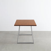 Gemoneの艶やかなチークブラウンのラバーウッド材と美しい質感が際立つベル型ステンレス脚を組み合わせた重厚感のあるテーブル（横向き）
