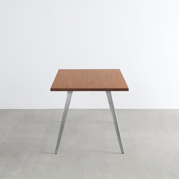 Gemoneの艶やかなチークブラウンのラバーウッド材と美しい質感が際立つフラットピンのステンレス脚を組み合わせた重厚感のあるテーブル(横からのアングル)