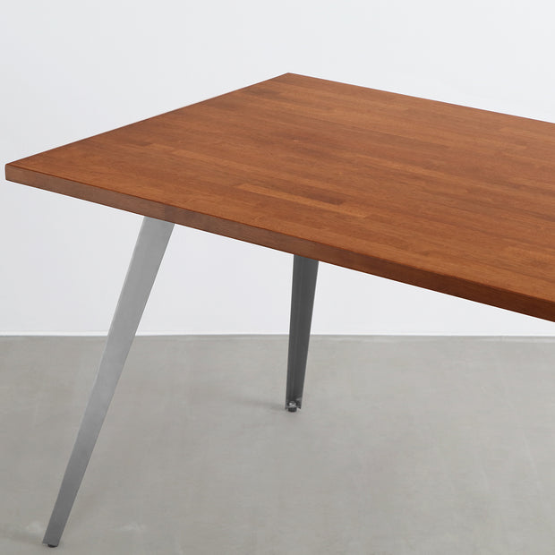 Gemoneの艶やかなチークブラウンのラバーウッド材と美しい質感が際立つフラットピンのステンレス脚を組み合わせた重厚感のあるテーブル(斜めからのアングル)