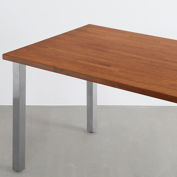Gemoneの艶やかなチークブラウンのラバーウッド材と美しい質感が際立つスクエアバーのステンレス脚を組み合わせた重厚感のあるテーブル(斜めからのアングル)