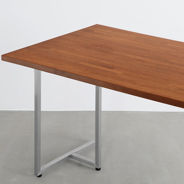 Gemoneの艶やかなチークブラウンのラバーウッド材と美しい質感が際立つT型ステンレス脚を組み合わせた重厚感のあるテーブル（斜め向き・クローズアップ）