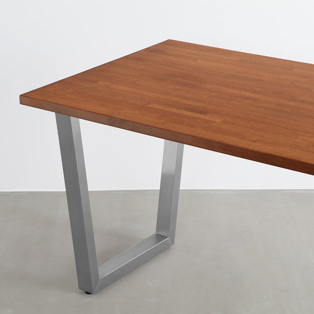 Gemoneの艶やかなチークブラウンのラバーウッド材と美しい質感が際立つトラペゾイドのステンレス脚を組み合わせた重厚感のあるテーブル(斜めからのアングル)